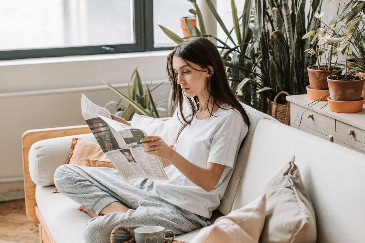 A woman relaxing at home on a sofa, surrounded by plants — home-visit homeopathy consultation