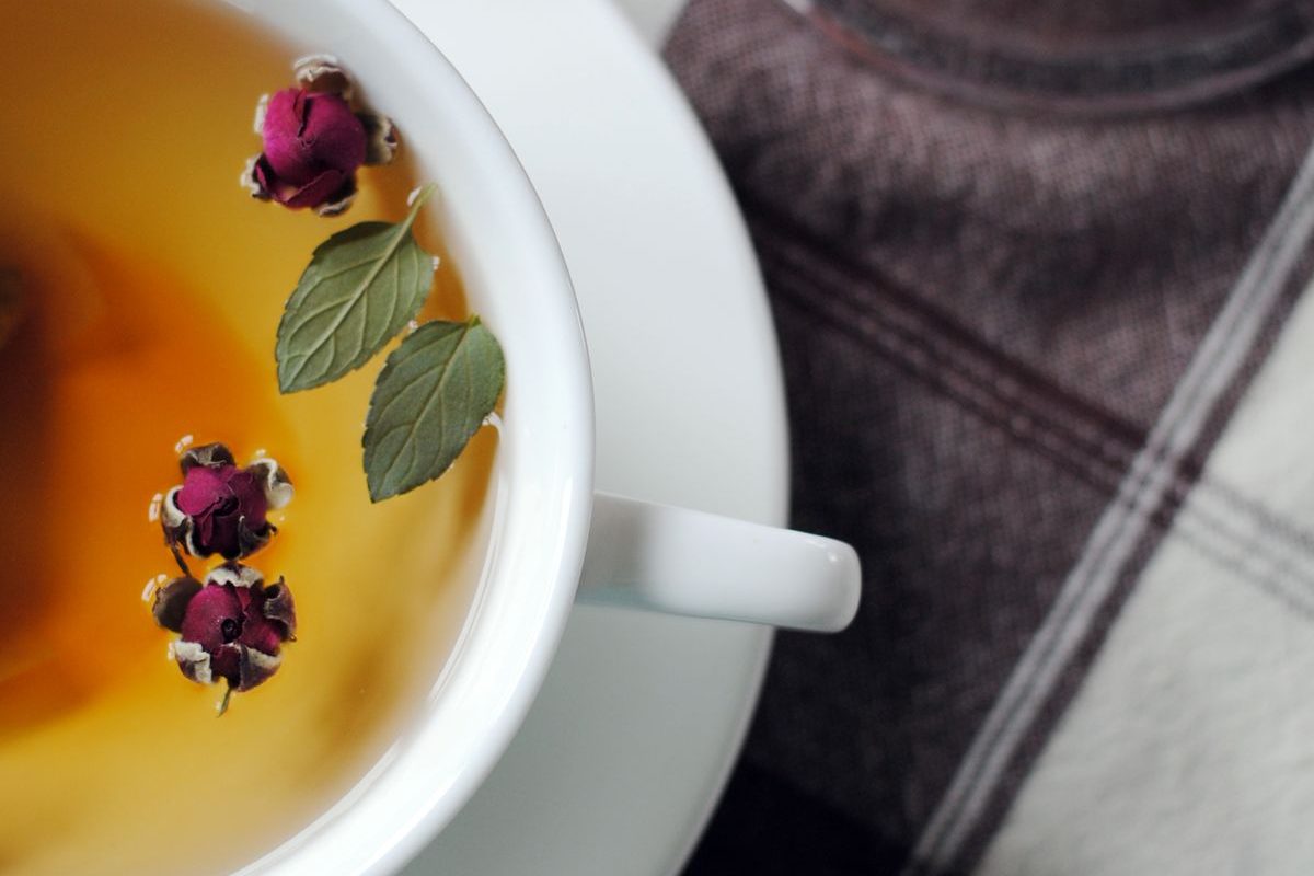 A cup of herbal tea with rosebuds and mint leaves